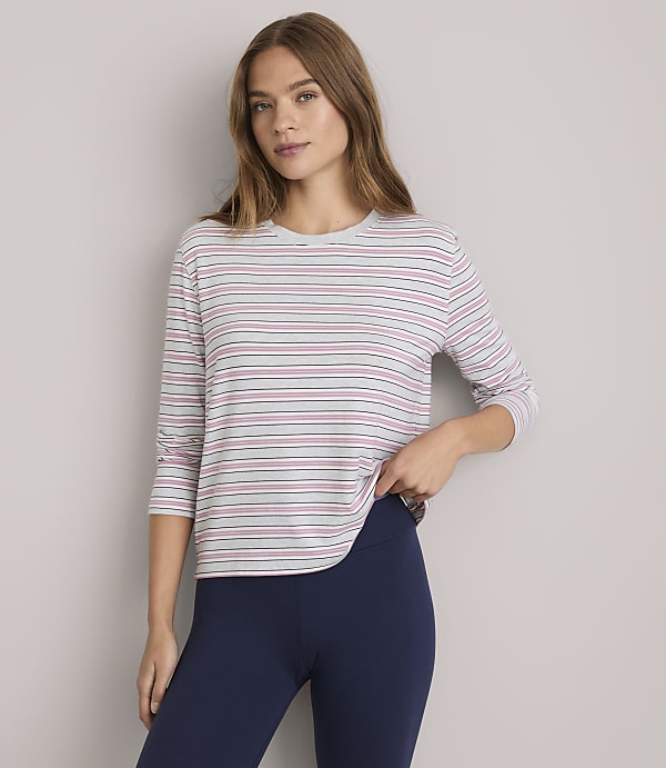 A woman in a striped shirt and navy leggings stands against a plain white background.