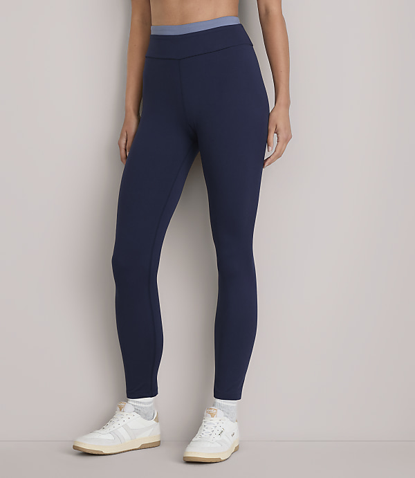 A person stands in dark blue leggings and white sneakers against a plain white background.