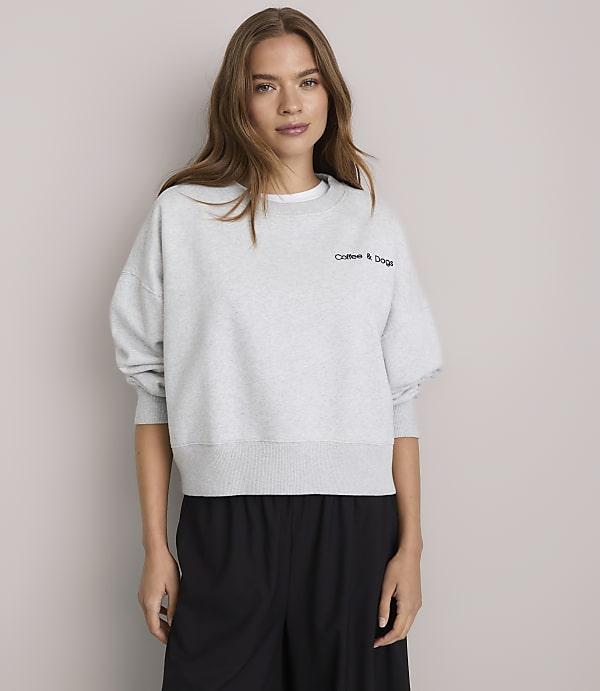 A young woman in a light gray sweatshirt stands against a plain white background.