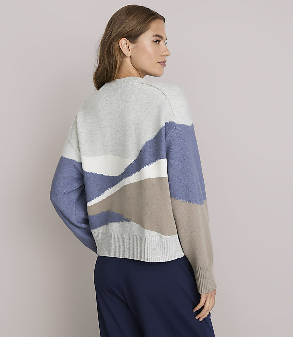 A woman in a patterned sweater stands against a plain background.