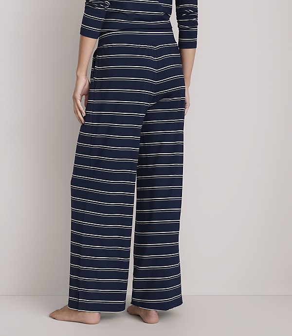 A person stands in wide-leg, navy and white striped pajama pants against a plain white background.