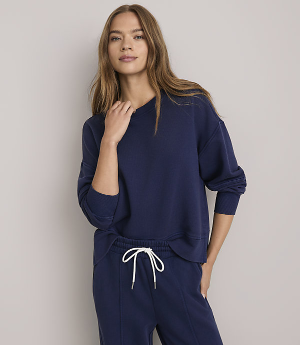 A woman in a navy blue sweatshirt and sweatpants stands against a plain white background.