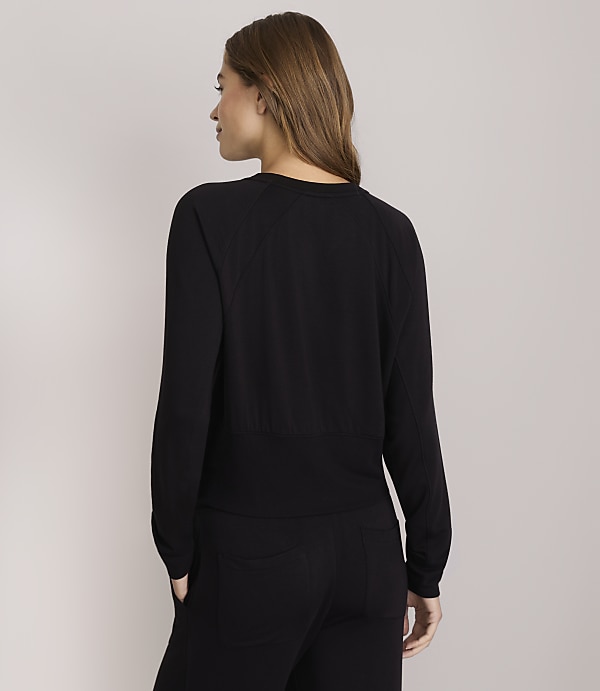 A woman in a black long-sleeved shirt and pants stands against a plain gray background.