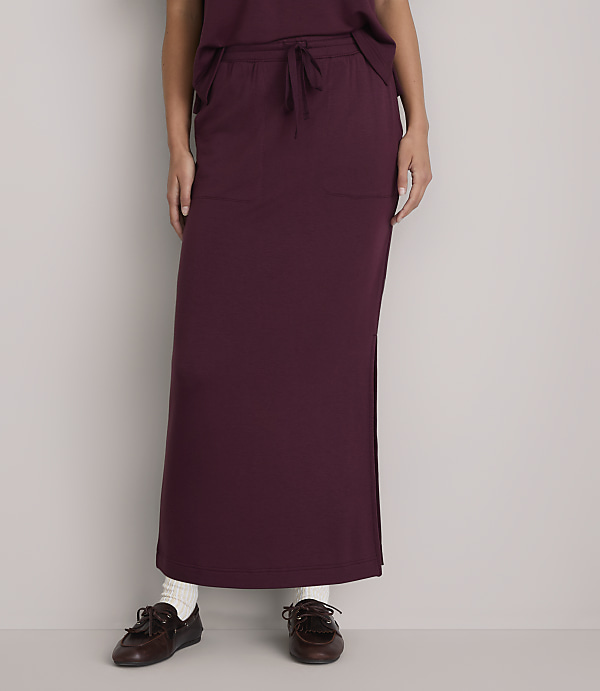 A person wearing a burgundy maxi skirt and brown loafers stands against a plain white background.