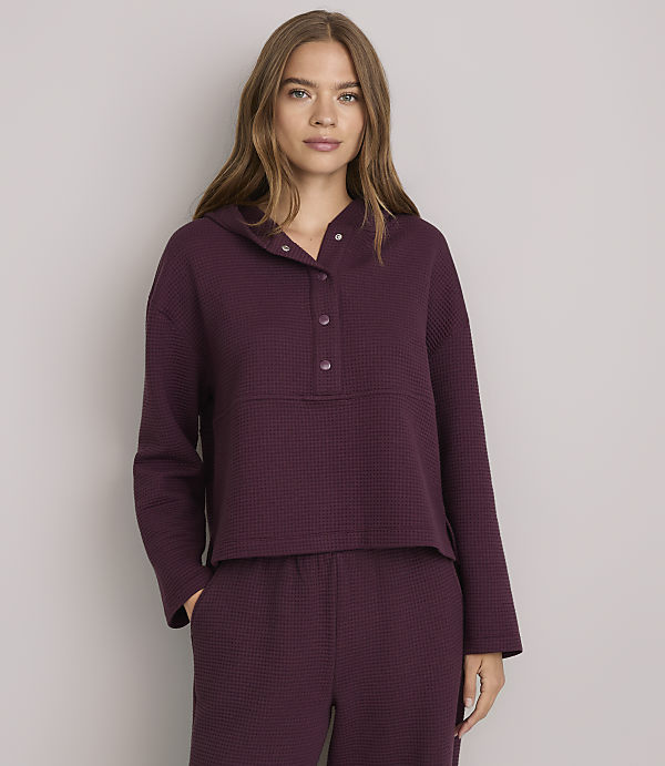 A woman in a burgundy waffle-knit hoodie and matching pants stands against a plain gray background.