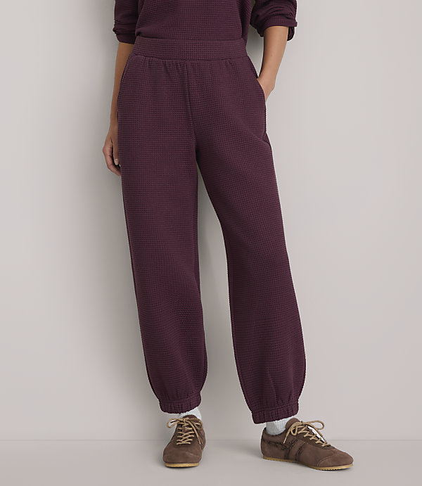 A person stands in maroon checkered sweatpants and brown sneakers against a plain white background.