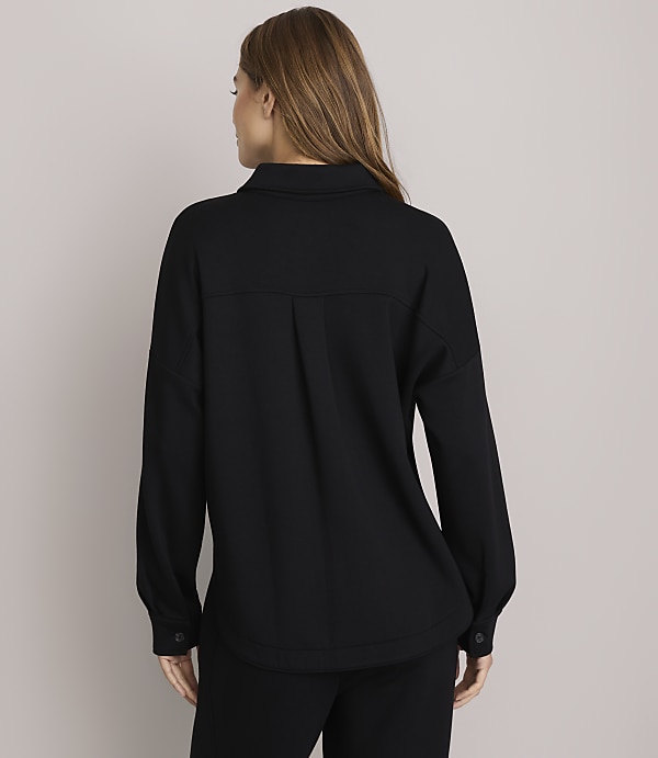 A woman in a black shirt and pants stands against a plain white background.
