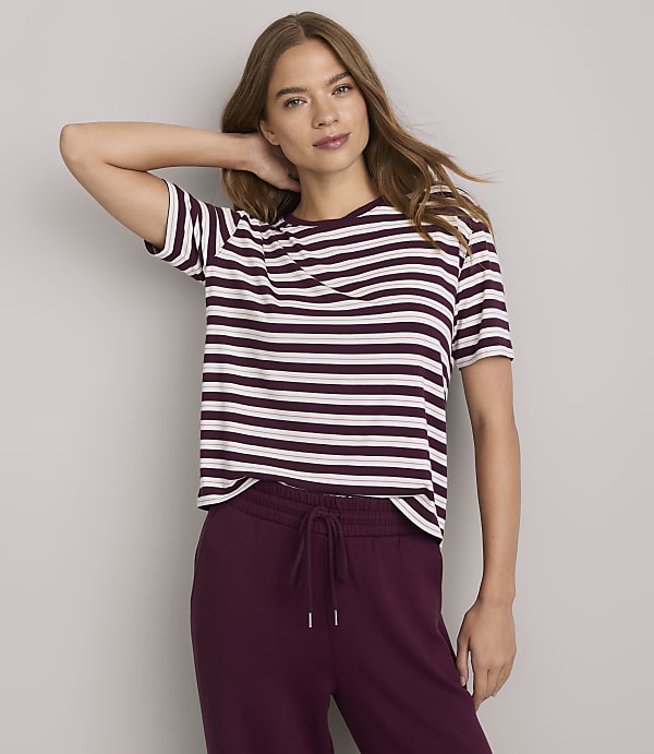 A woman in a striped t-shirt and maroon sweatpants poses against a plain gray background.