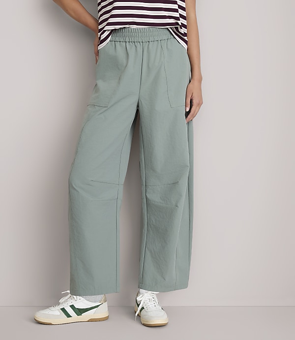 A person stands in light green wide-leg pants and white sneakers against a plain white background.