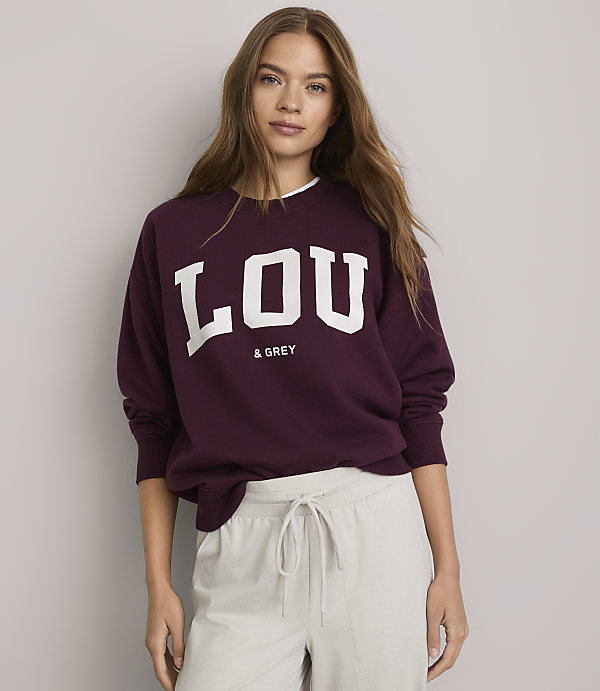 A young woman in a maroon sweatshirt with "LOU & GREY" printed on it stands against a plain white background.