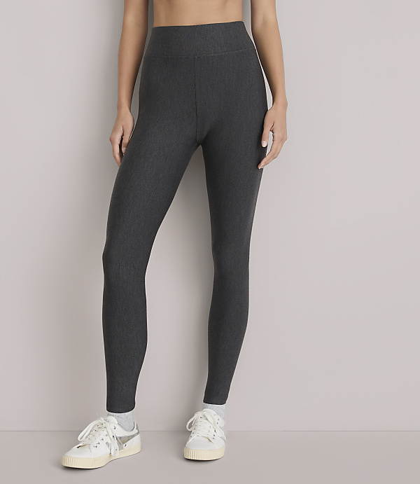 A person wearing dark grey ribbed leggings and white sneakers stands against a plain white background.