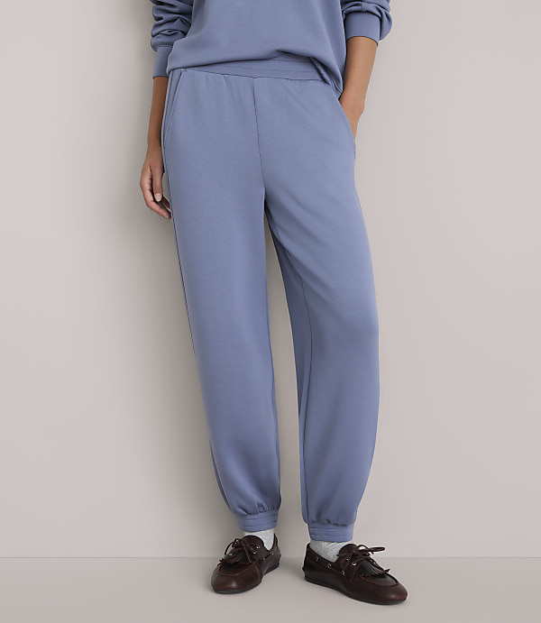 A person wearing blue sweatpants and brown loafers stands against a plain white background.