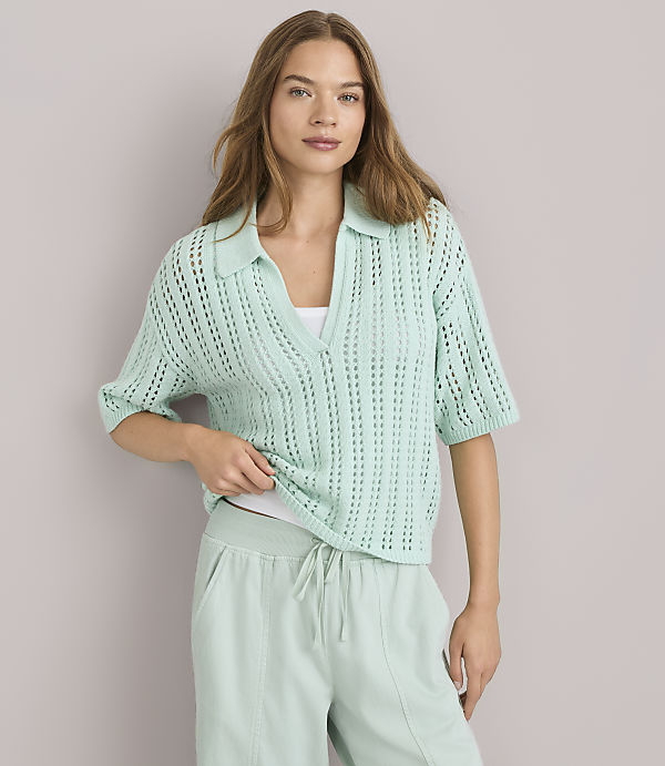 A woman in a light green collared knit shirt and matching sweatpants stands against a plain gray background.
