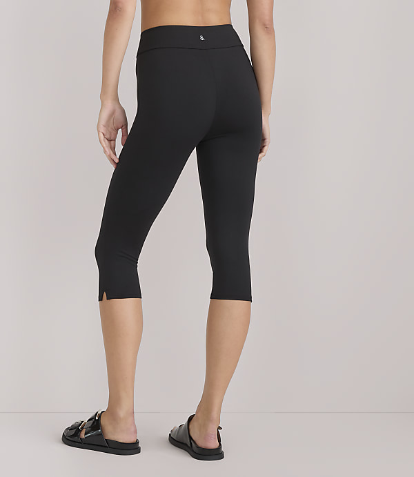 A person wearing black capri leggings and sandals stands against a plain white background.