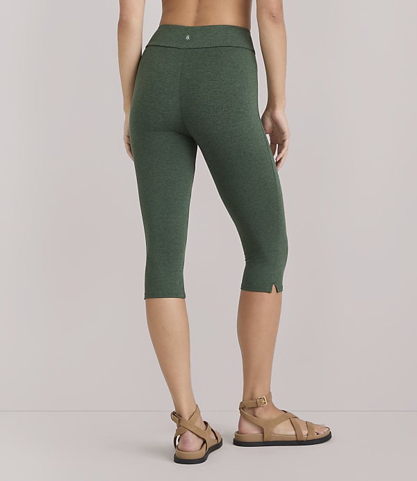 A woman in green capri leggings and sandals stands against a plain white background.