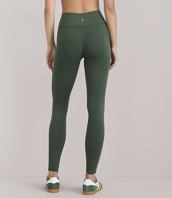 A woman wearing green heathered leggings and white-and-green sneakers stands against a plain white background.