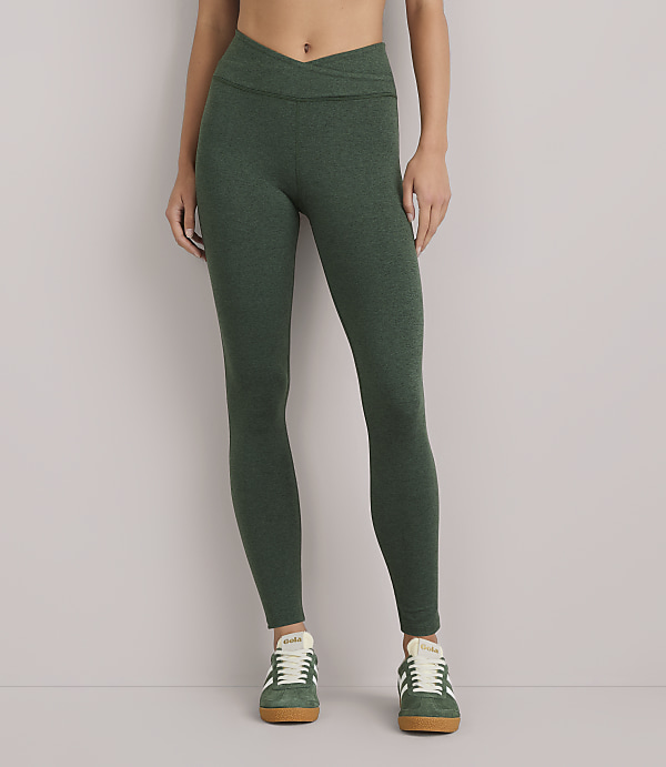 A person wearing green heathered leggings and green sneakers stands against a plain white background.