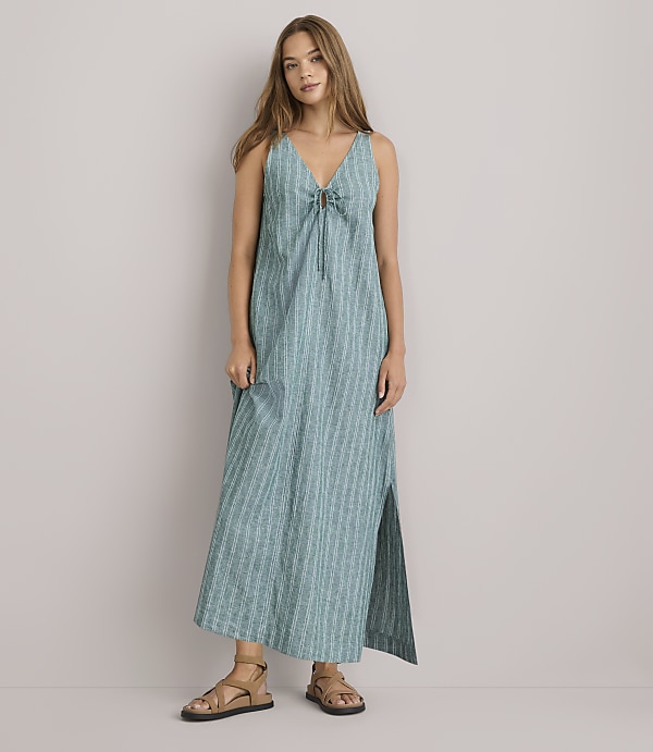 A young woman in a green striped dress stands with her arms crossed against a plain white background.