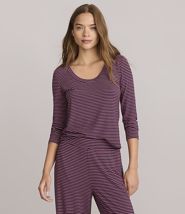 A woman in a striped top and pants stands against a plain gray background.