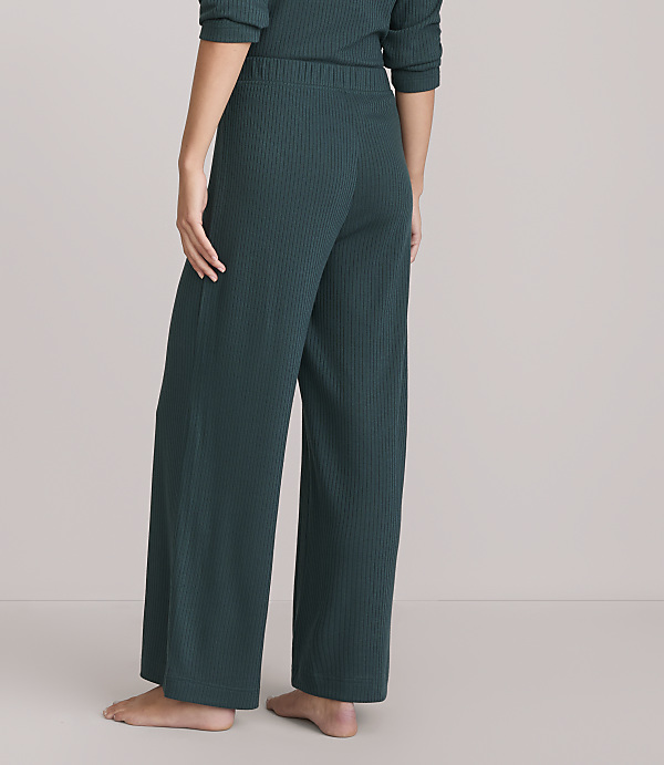 A person stands in dark green ribbed pajamas, with a plain white background.