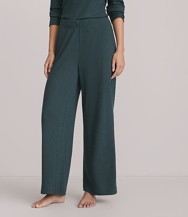 A person stands in dark green ribbed wide-leg pants against a plain white background.