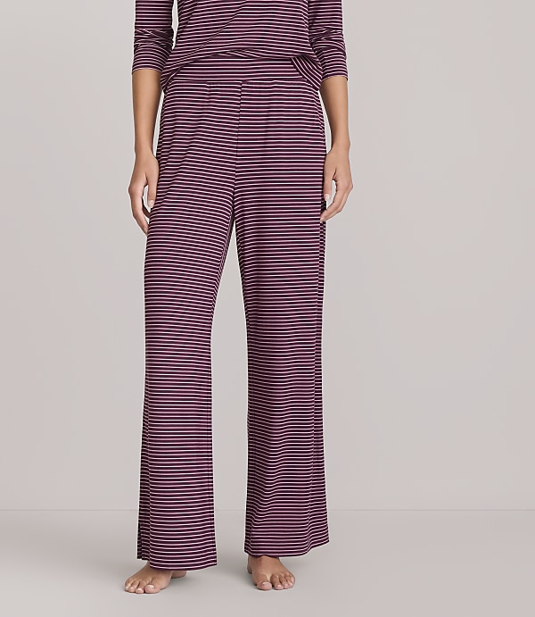 A person stands wearing burgundy and navy striped pajama pants and a matching top against a plain white background.