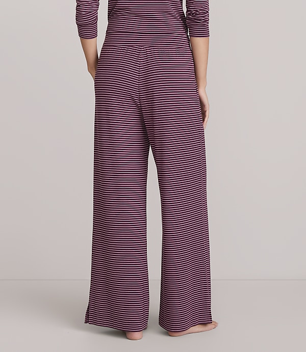 A person stands in wide-leg striped pajama pants against a plain, light gray background.