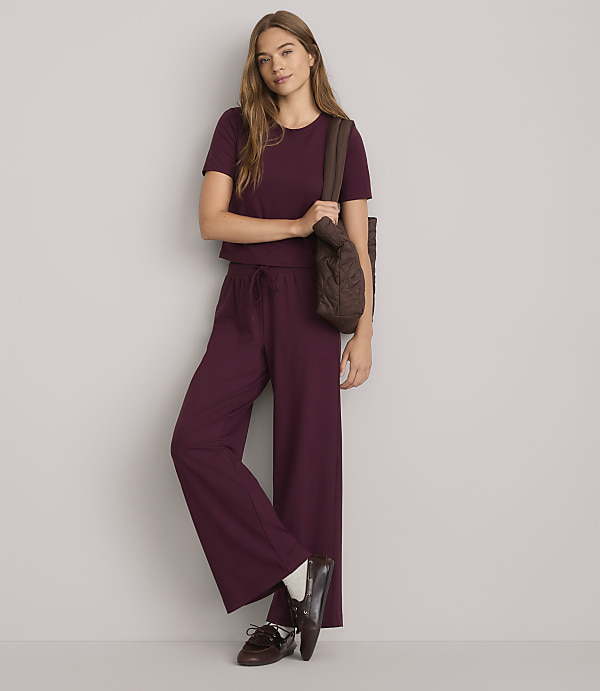 A young woman in a burgundy loungewear set and brown loafers stands against a plain white background, carrying a quilted brown tote bag.