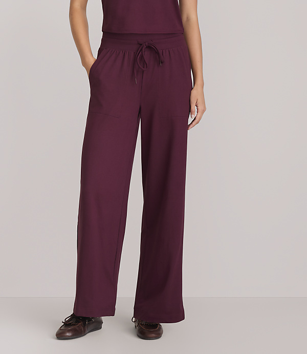 A person wearing maroon wide-leg pants and brown shoes stands against a plain gray background.
