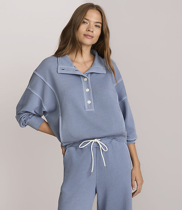 A woman in a blue sweatshirt and matching pants stands against a plain white background.
