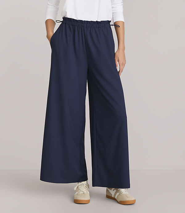 A person stands in dark blue wide-leg pants and white sneakers against a plain white background.