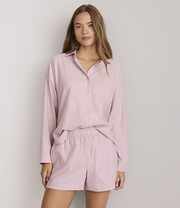 A woman in pink and white striped pajamas stands against a plain white background.