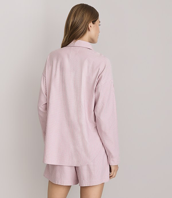 A woman in pink and white striped pajamas stands against a plain white background.