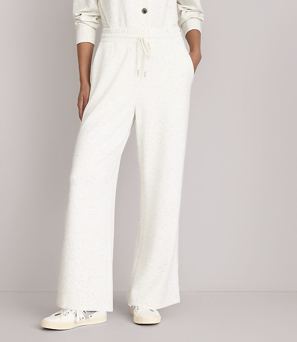 A person stands in cream-colored wide-leg pants and sneakers against a plain white background.