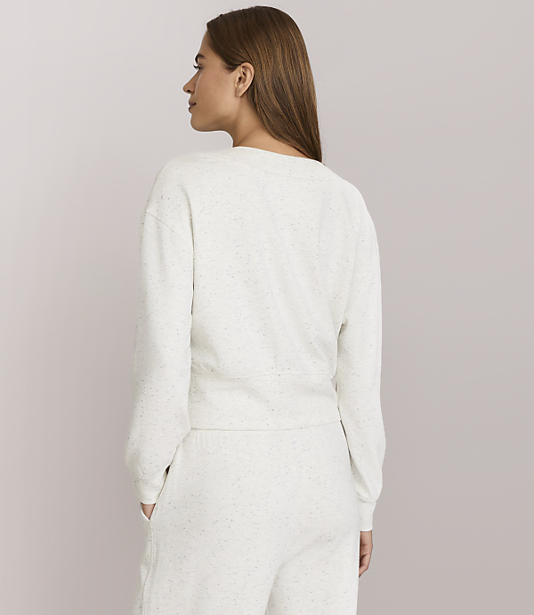 A woman in a light-colored sweatshirt and sweatpants stands with her back to the camera against a plain, light gray background.