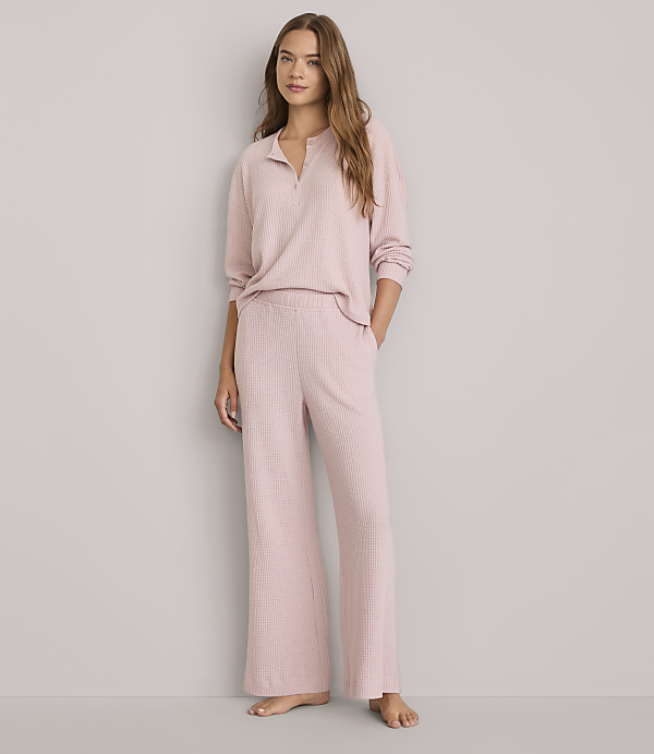 A woman in a pink pajama set stands against a plain gray background.