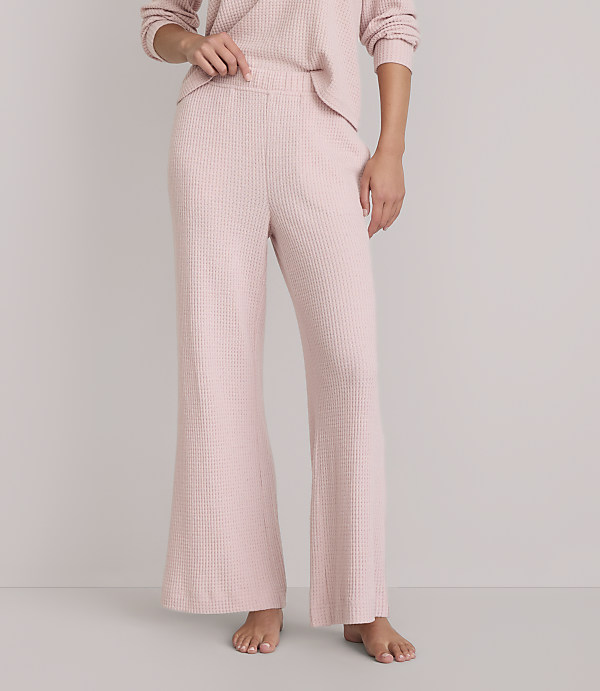 A person stands barefoot in pink waffle-knit pajama pants and a matching top against a plain white background.
