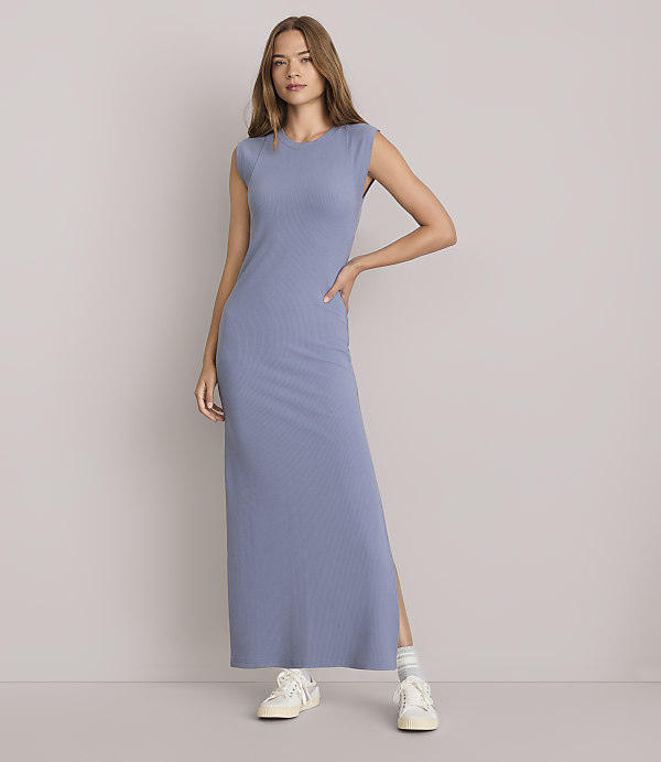 A woman in a blue ribbed maxi dress stands against a plain white background.
