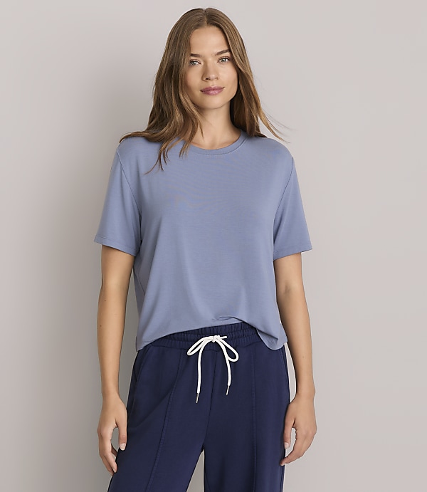 A woman in a blue t-shirt and navy pants stands against a plain gray background.