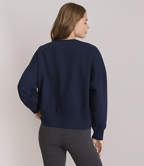 A woman in a navy sweatshirt and grey leggings stands against a plain white background.