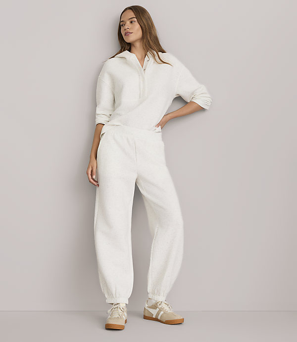 A woman in a cream-colored loungewear set stands against a plain gray background.