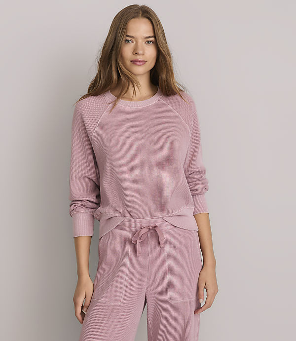 A woman in a pink waffle-knit loungewear set stands against a plain gray background.