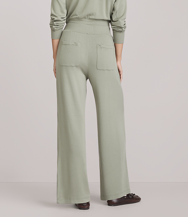 A person wearing light green wide-leg pants and brown loafers stands against a plain white background.