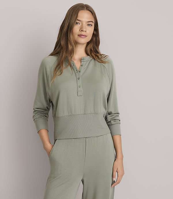 A woman in a green henley shirt and matching pants stands against a plain gray background.