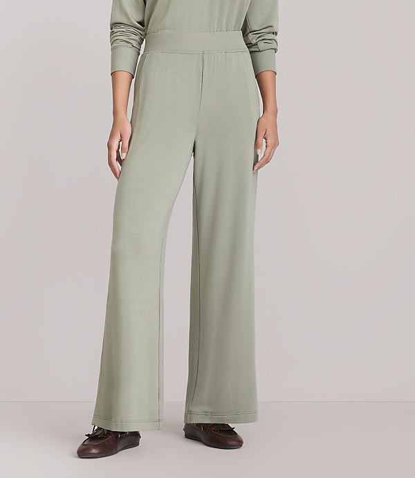 A person wearing light green wide-leg pants and brown loafers stands against a plain white background.