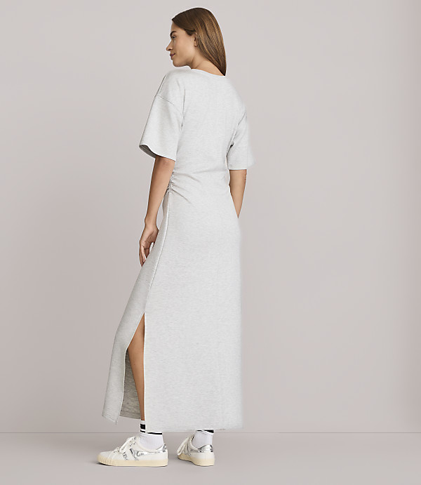 A woman in a grey maxi dress and sneakers stands against a plain grey background.