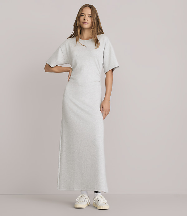 A woman in a light gray maxi t-shirt dress stands against a plain white background.