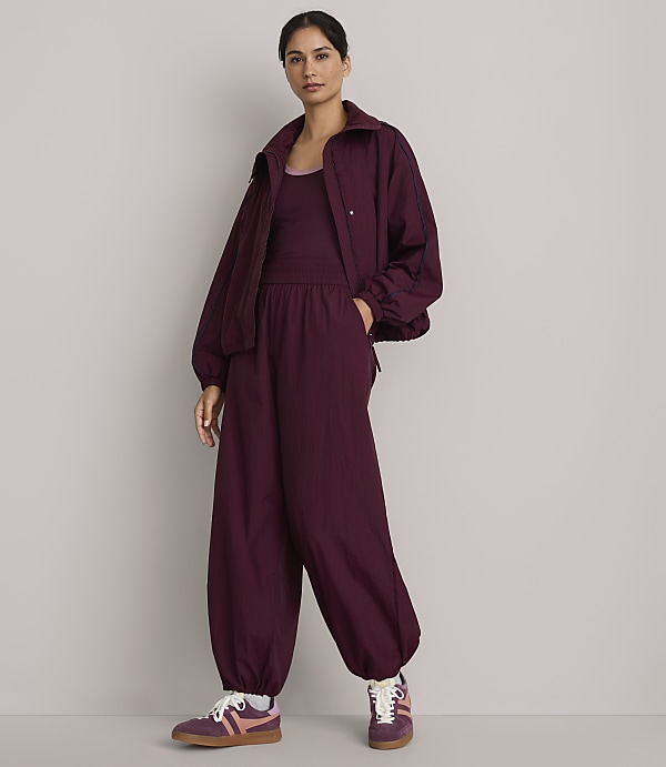 A woman in a burgundy tracksuit stands against a plain gray background.