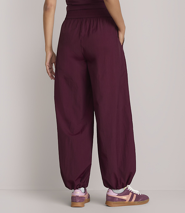 A person wearing loose-fitting burgundy pants and sneakers stands against a plain, light-colored background.