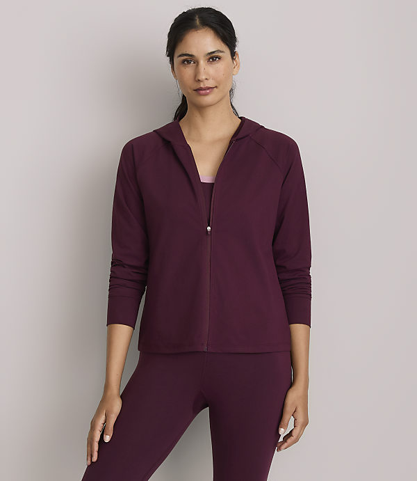 A woman in a burgundy hooded jacket and matching leggings stands against a plain gray background.